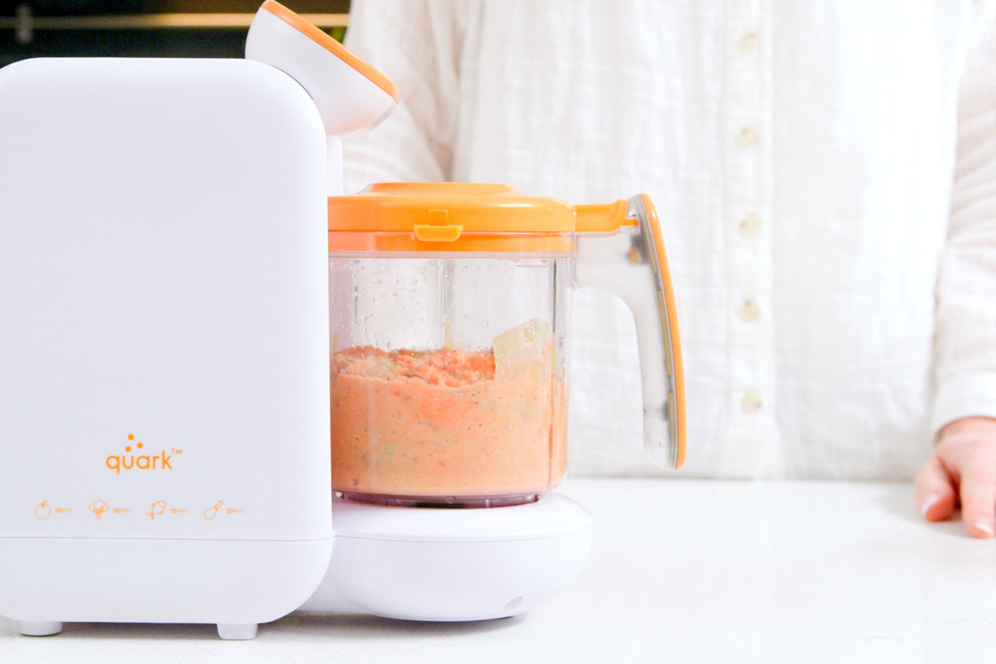 Quark Baby food processor with orange lid containing blended baby food puree in kitchen setting.