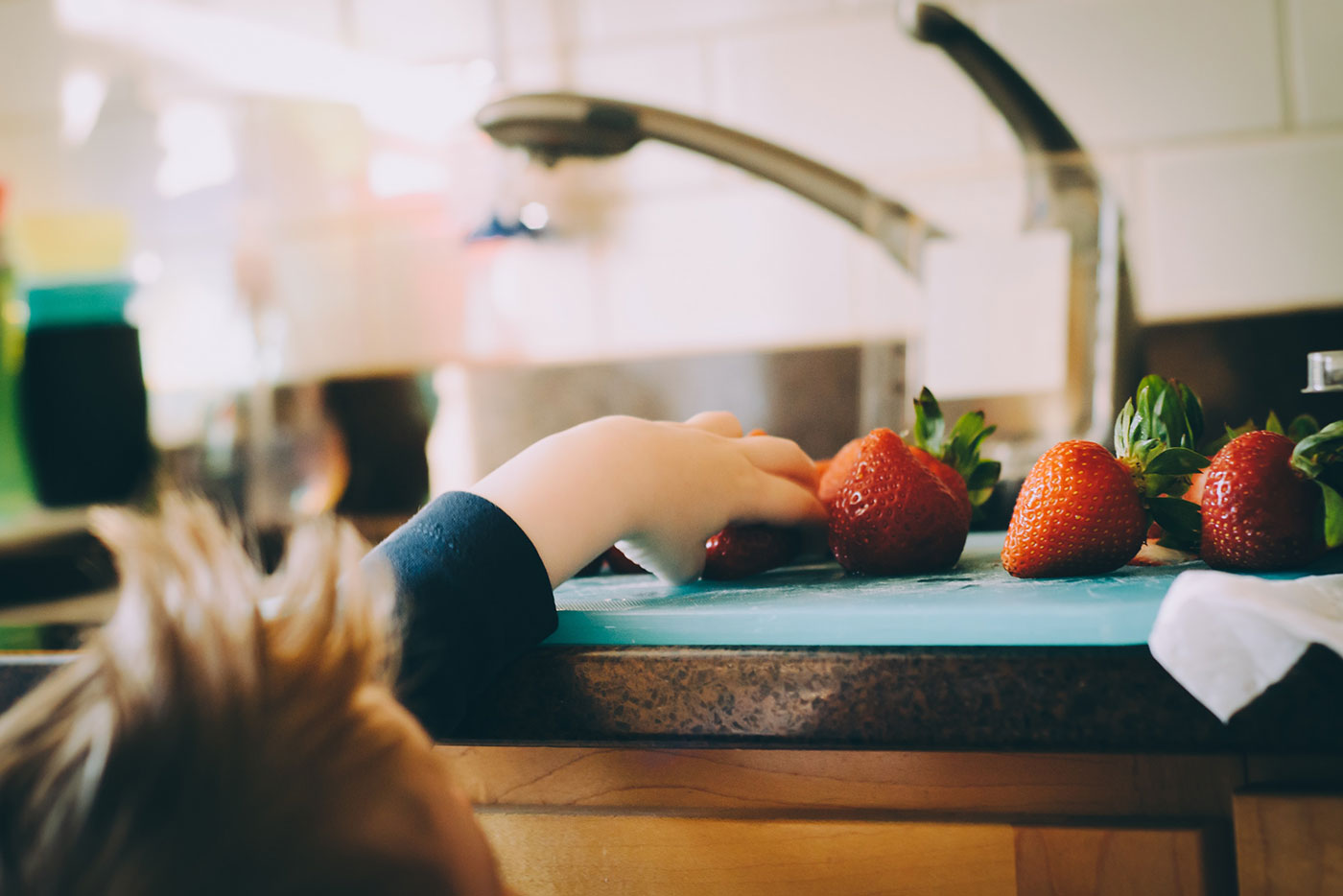 Child's hand reaching for fresh strawberries on Quark Baby feeding tray in kitchen.