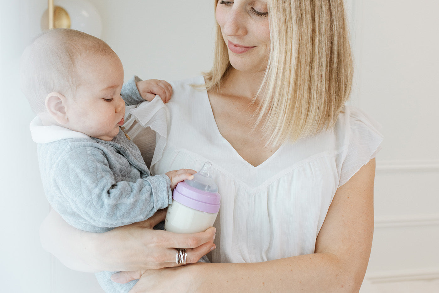 Mother holding Quark Baby bottle while feeding infant, combination feeding lifestyle shot