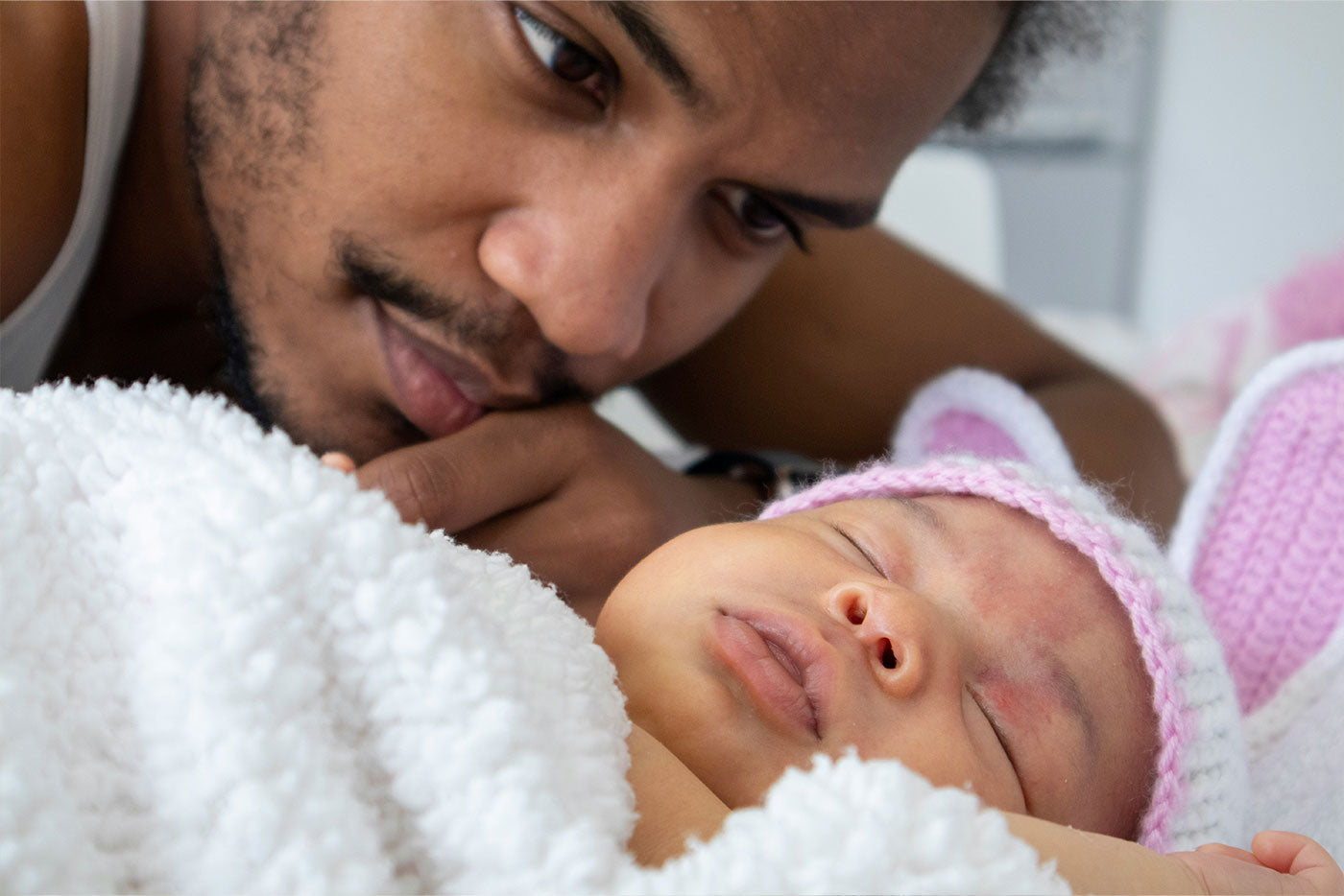 Father gazing at sleeping newborn wrapped in white blanket and pink hat, Quark Baby feeding lifestyle