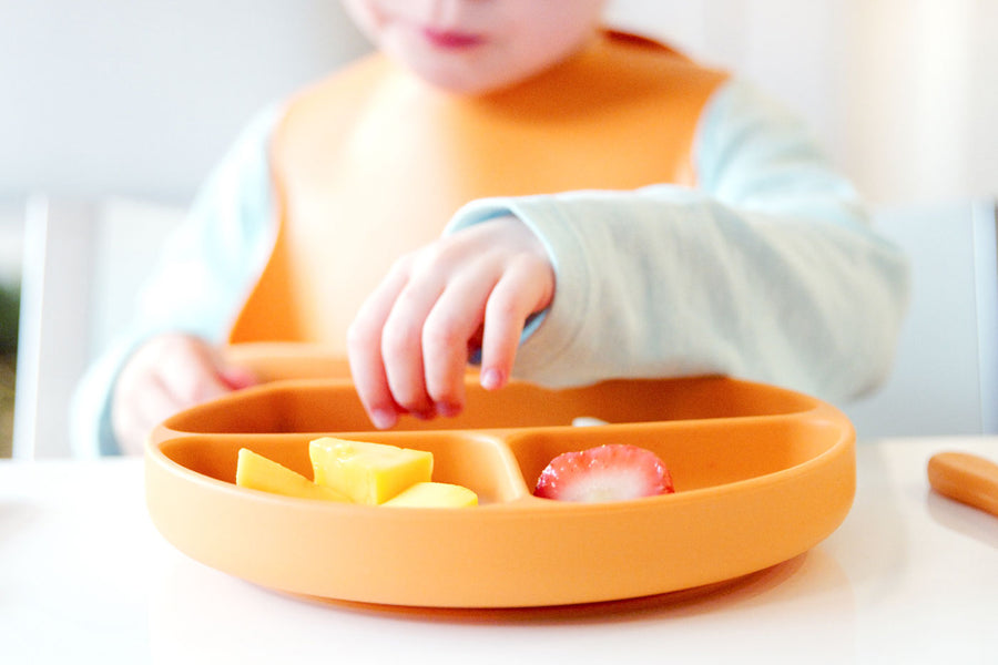 Quark Baby orange divided plate with toddler self-feeding finger foods during baby-led weaning.