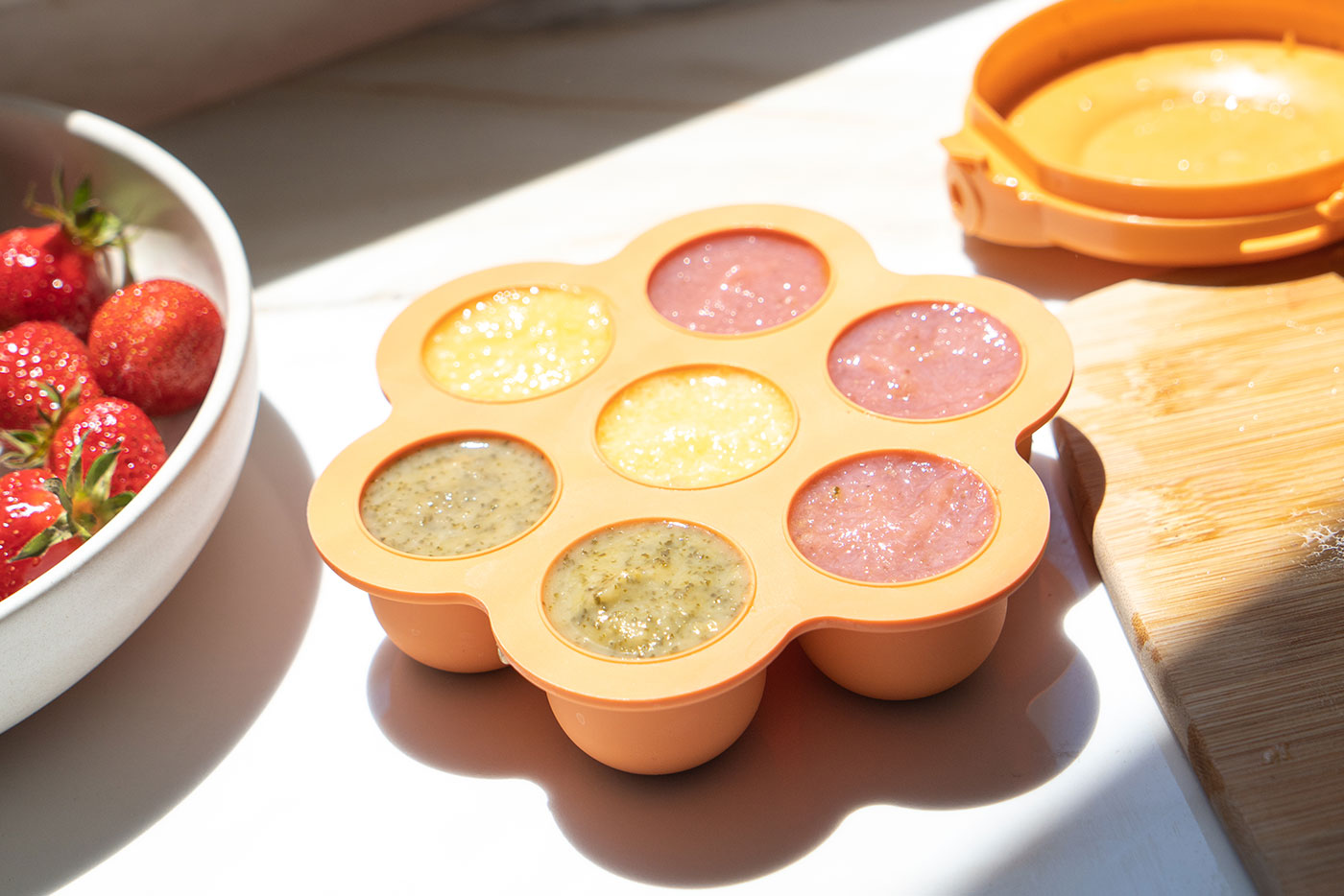 Quark Baby colorful baby food storage containers with fresh strawberries and bamboo spoon nearby.