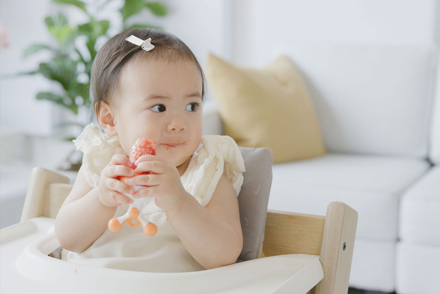 Toddler eating strawberry with Quark Baby fruit feeder in bright home setting