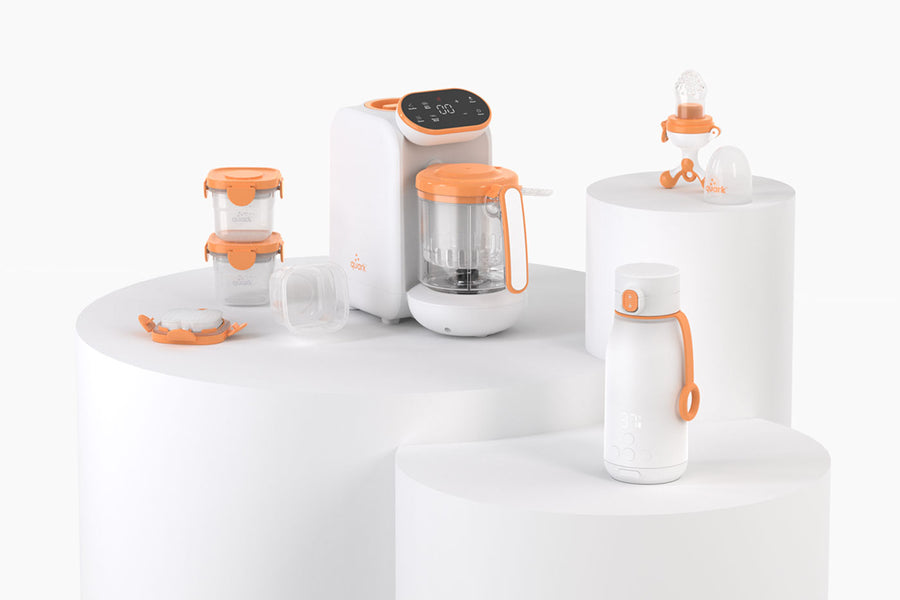 Quark Baby innovative feeding accessories collection with orange accents displayed on white pedestals.