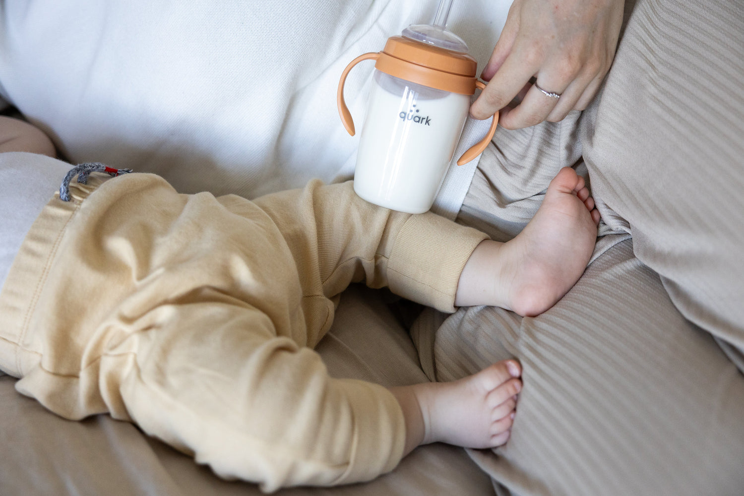 Adult holding Quark Baby orange sippy cup while feeding infant in lifestyle feeding scene.