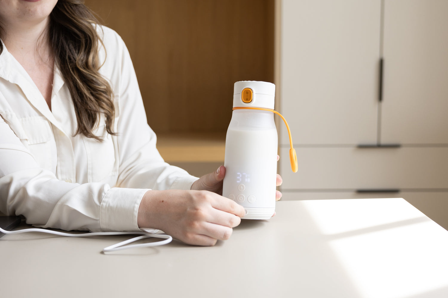 Woman presenting Quark Baby white bottle with yellow accent on table in pumping at work lifestyle setting.