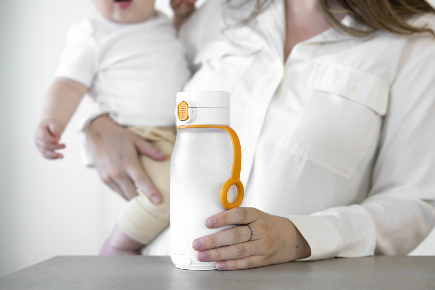 Adult holding white Quark Baby bottle while feeding infant in neutral setting.