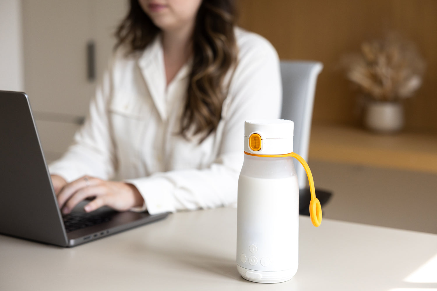 Quark Baby white bottle with yellow carry handle on desk near working parent with laptop