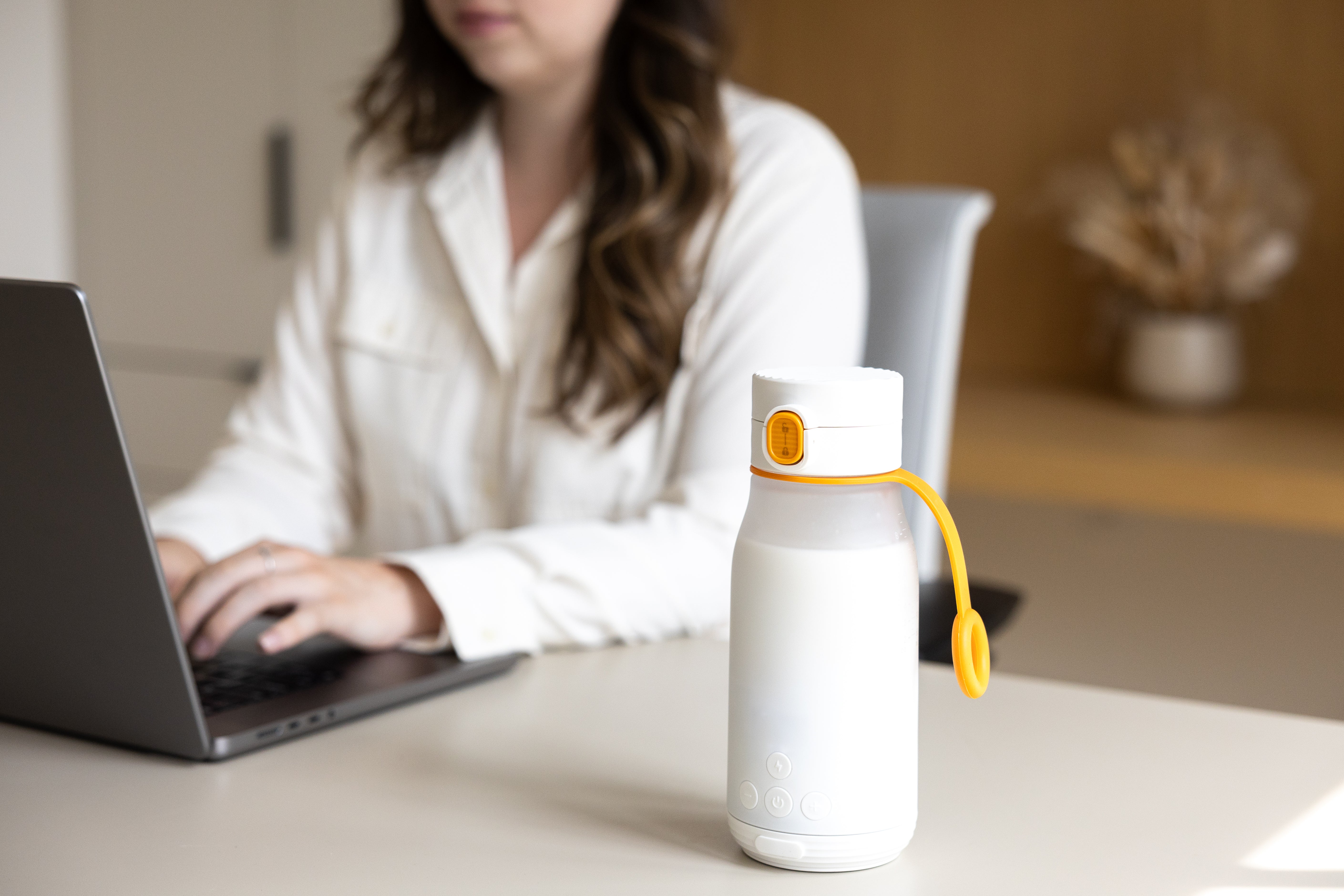 Quark Baby white bottle with yellow carry handle on desk near working parent with laptop