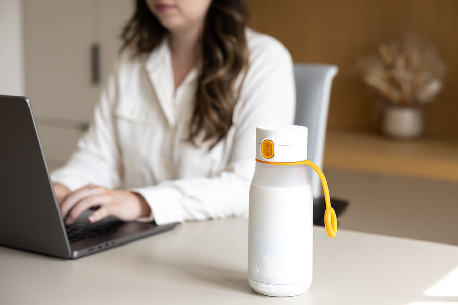 Quark Baby white bottle with yellow carry handle on desk near working parent with laptop