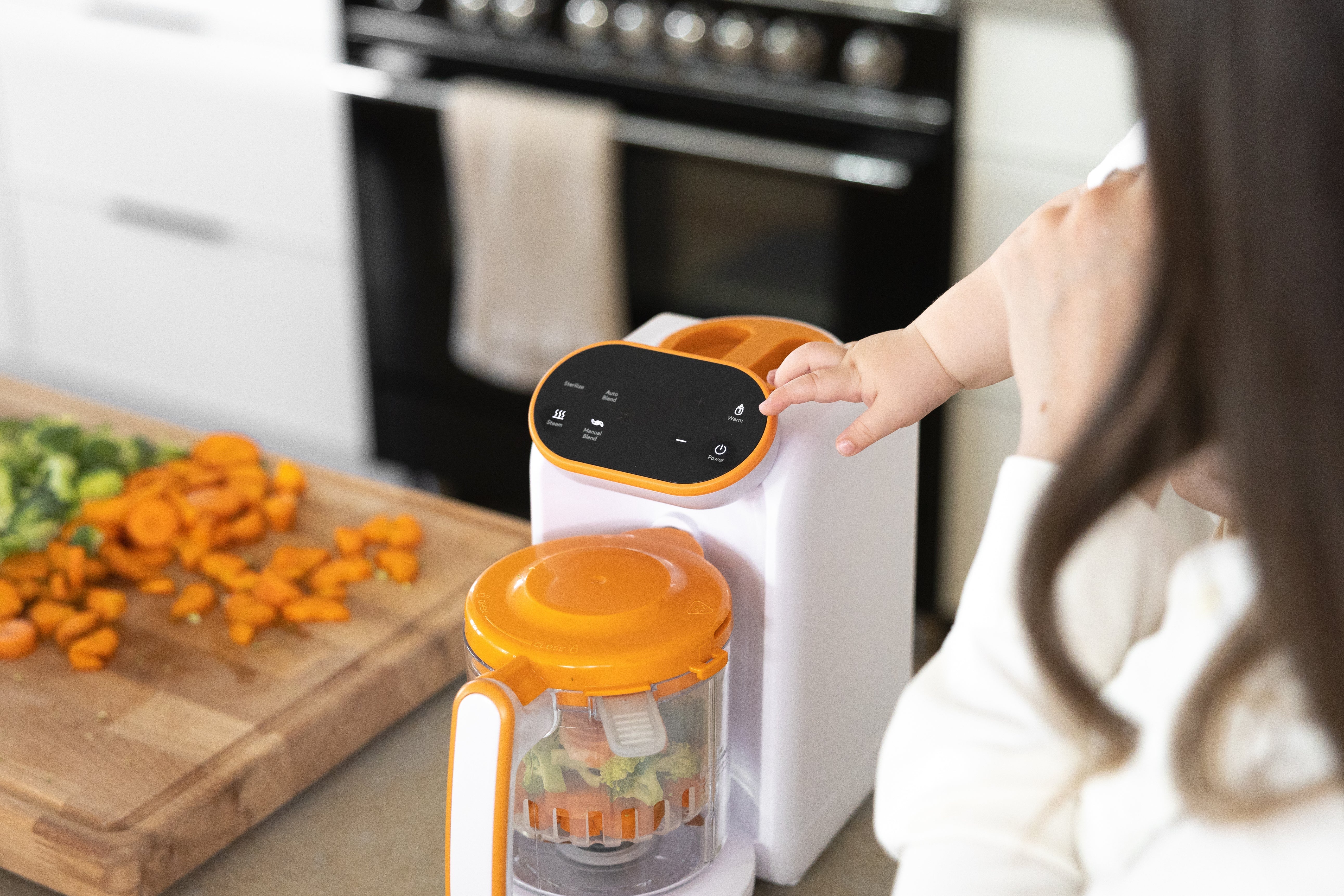 Woman's hand operating Quark Baby food processor with orange lid in kitchen.