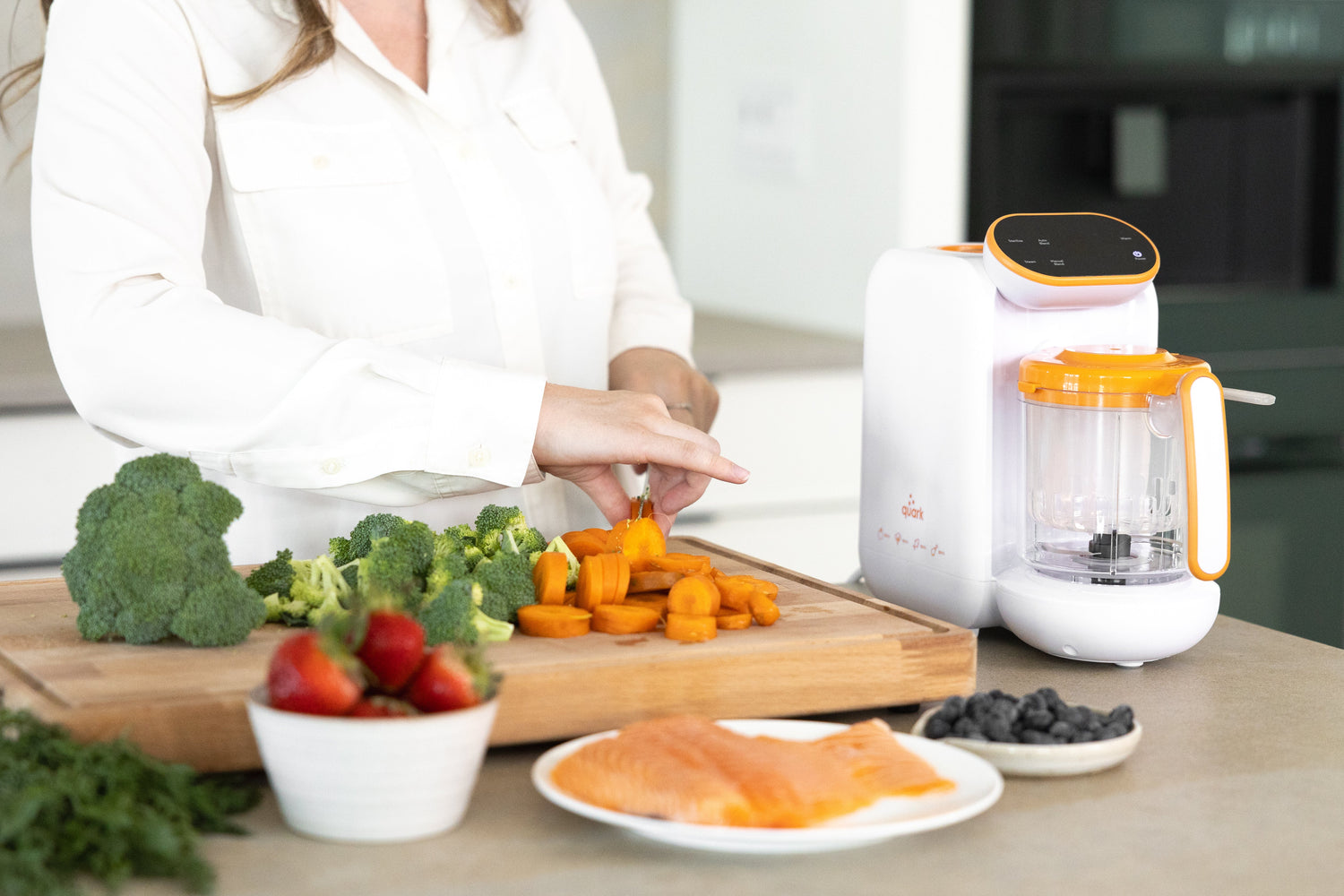 Woman preparing homemade baby food with Quark Baby food processor and fresh vegetables on cutting board.