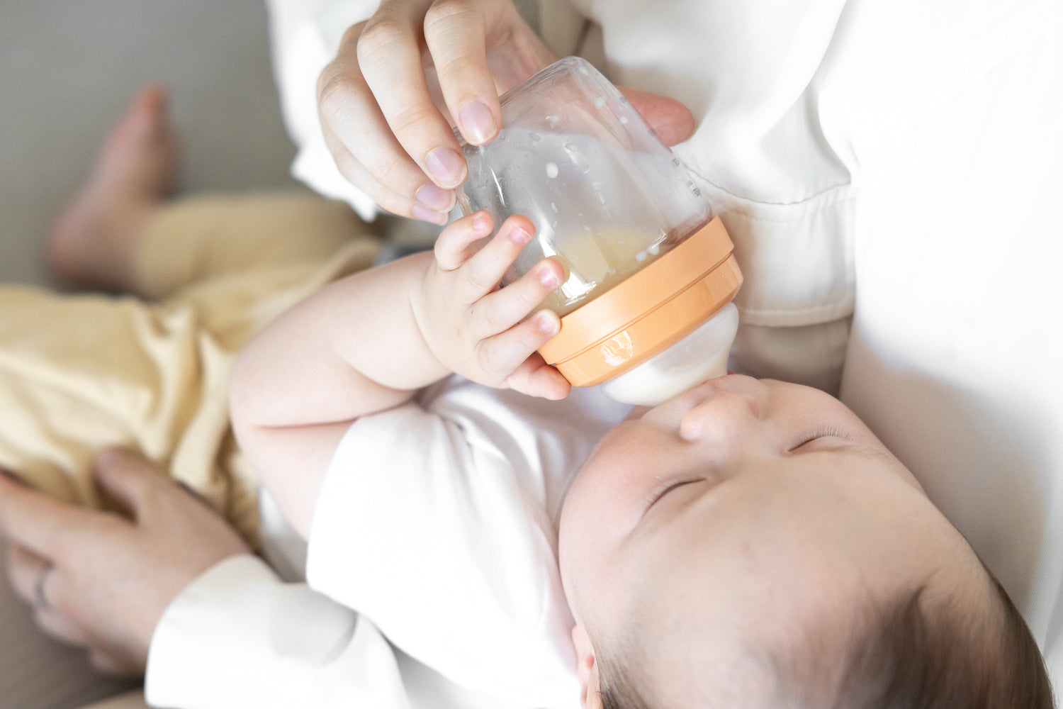 Adult feeding newborn with Quark Baby bottle during gentle feeding session.