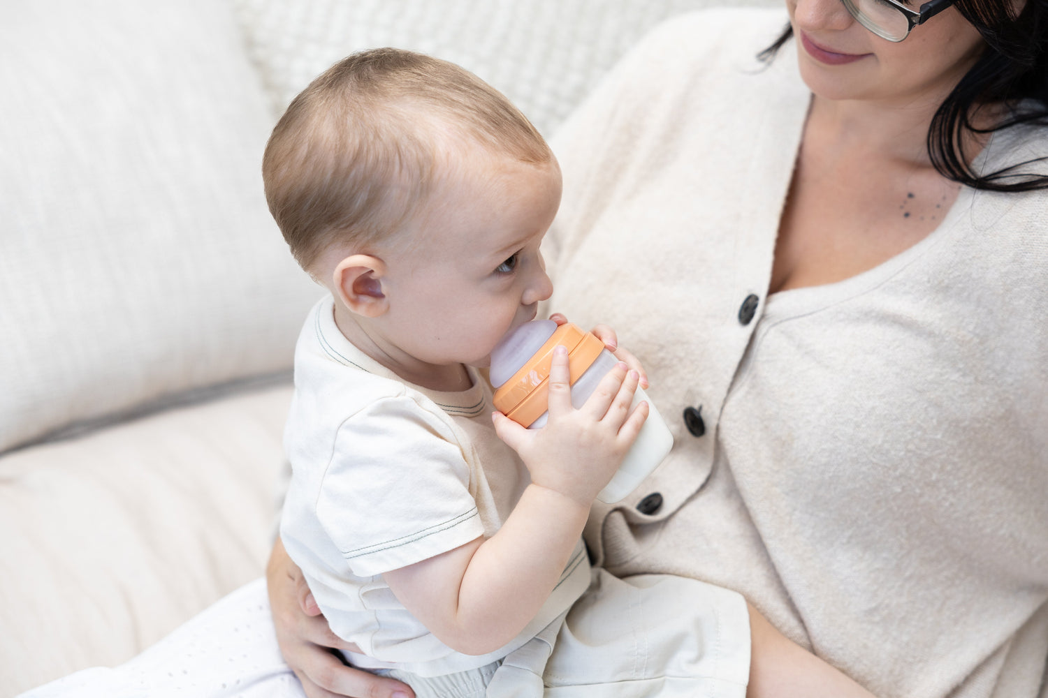 Adult feeding infant with Quark Baby orange bottle during formula feeding time