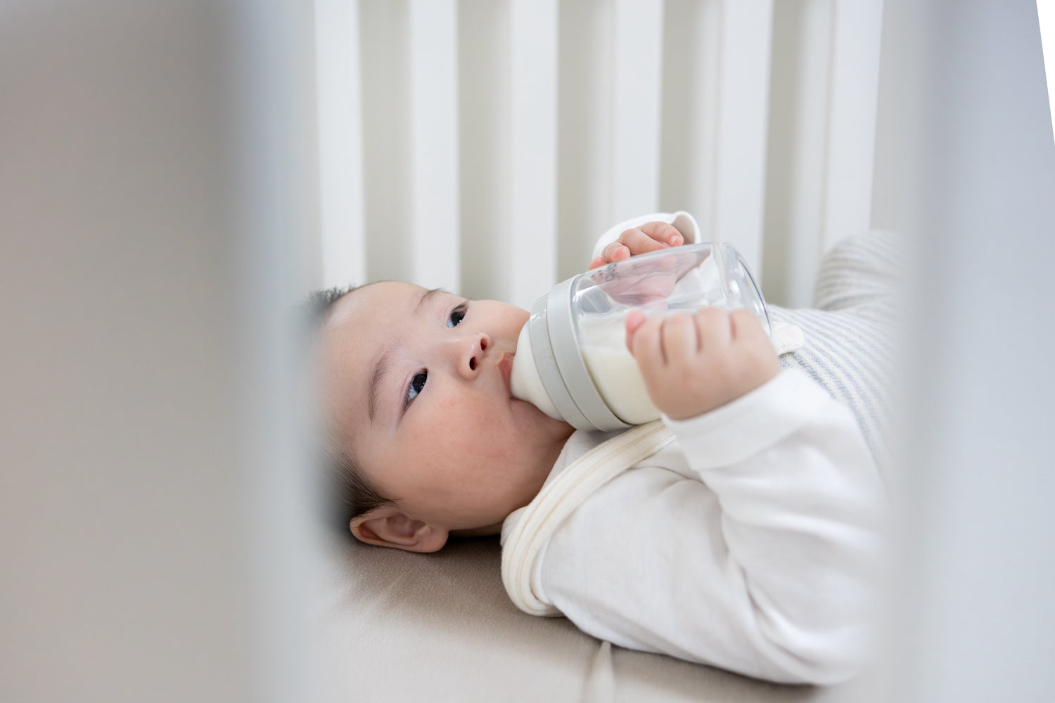 Infant drinking from bottle while lying in crib, Quark Baby feeding lifestyle shot