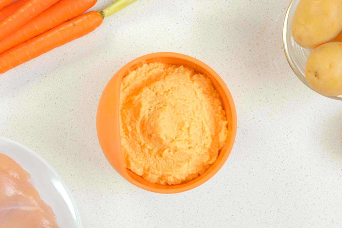 Quark Baby chicken, potato and carrot purée in orange bowl with fresh ingredients
