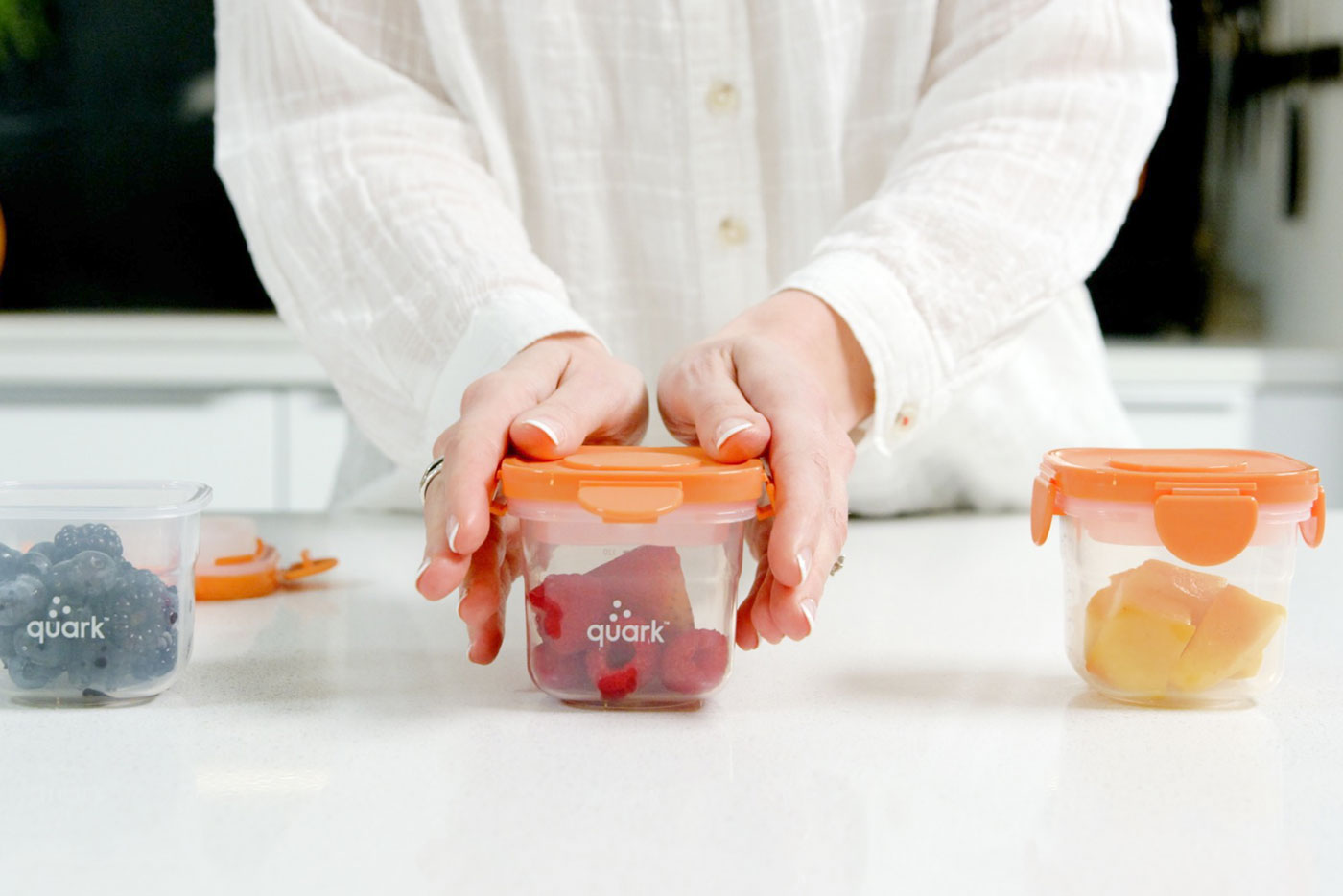 Woman presenting three Quark Baby storage containers with fresh berries and fruit for snack storage.
