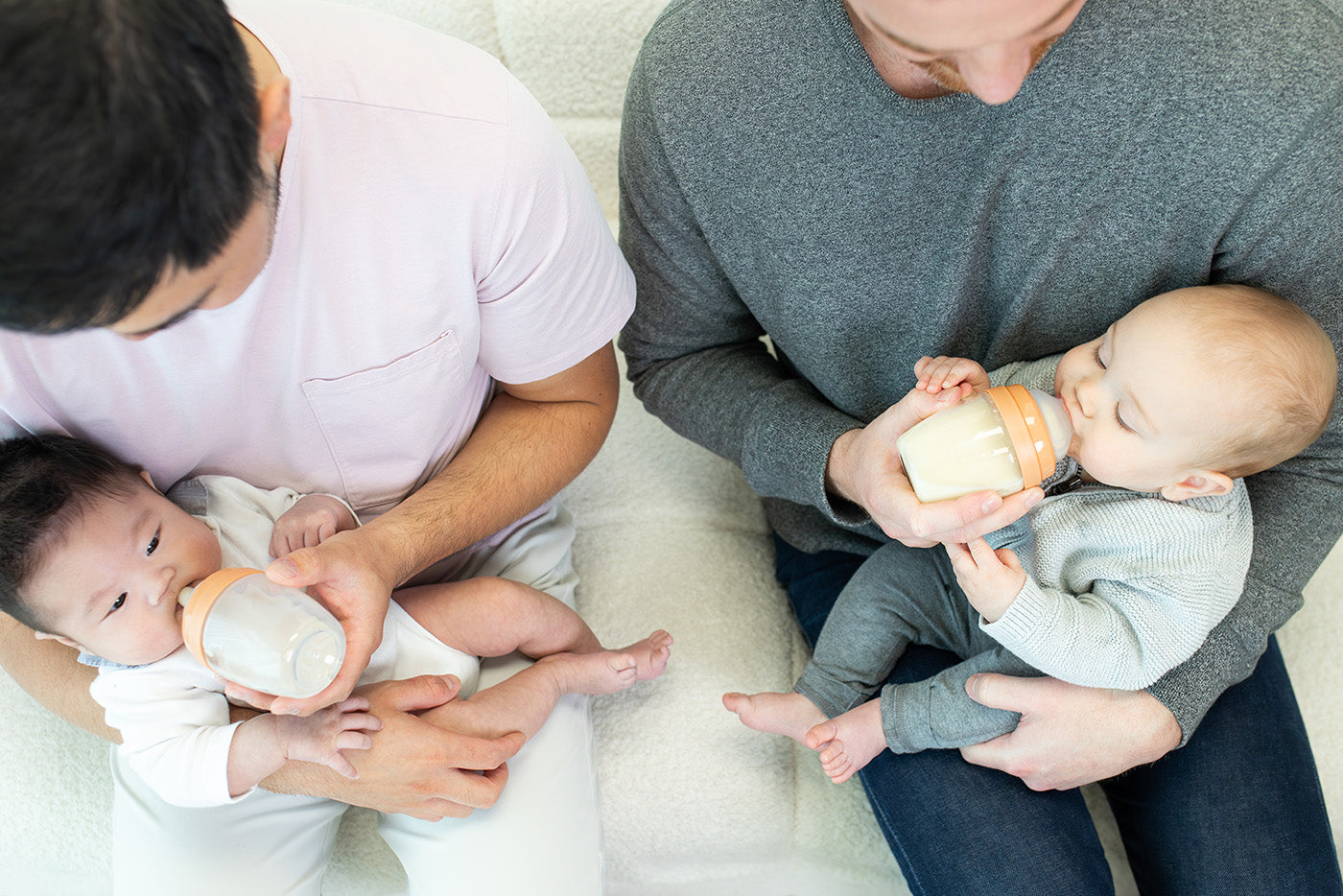 Two adults feeding infants with Quark Baby bottles in lifestyle scene.