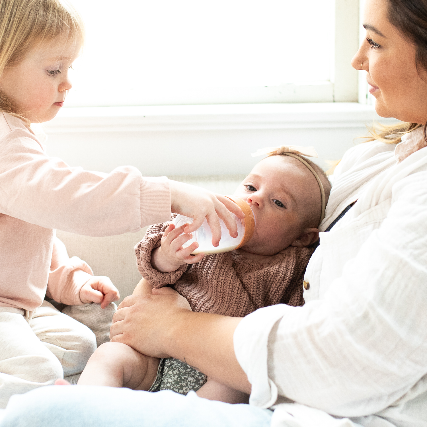 Woman feeding infant with bottle while toddler watches in Quark Baby lifestyle scene