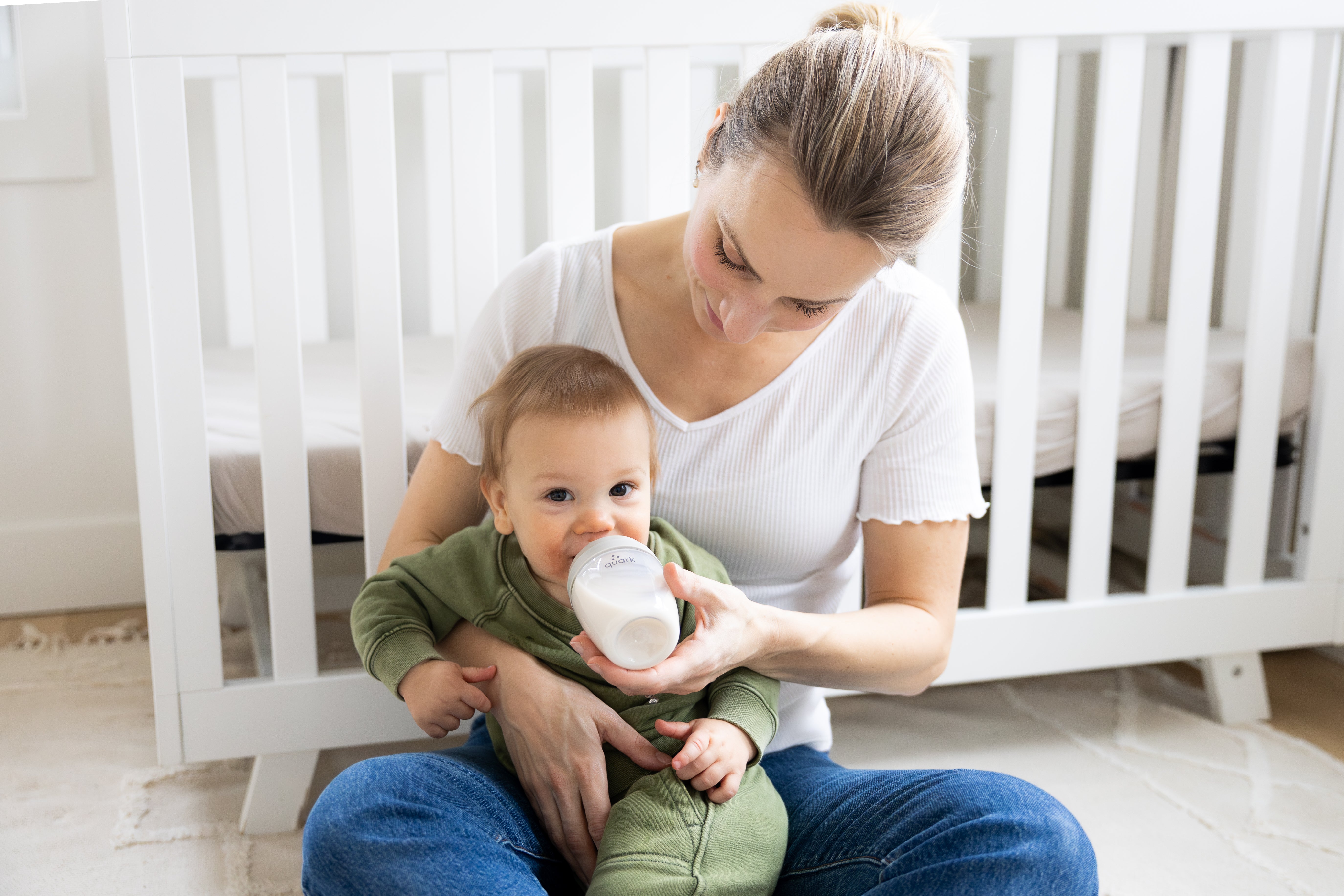 Mother feeding infant with Quark Baby bottle in nursery setting