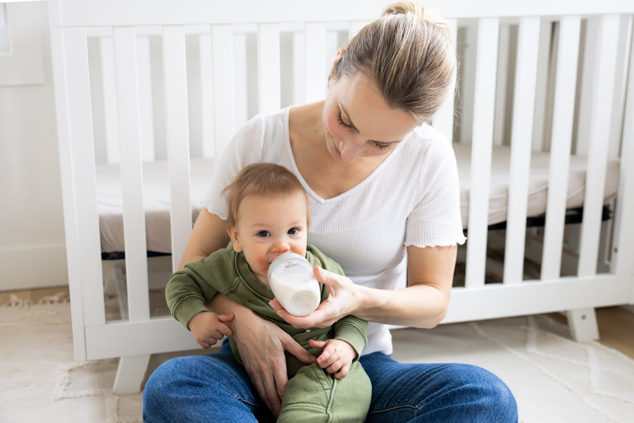 Mother feeding infant with Quark Baby bottle in nursery setting