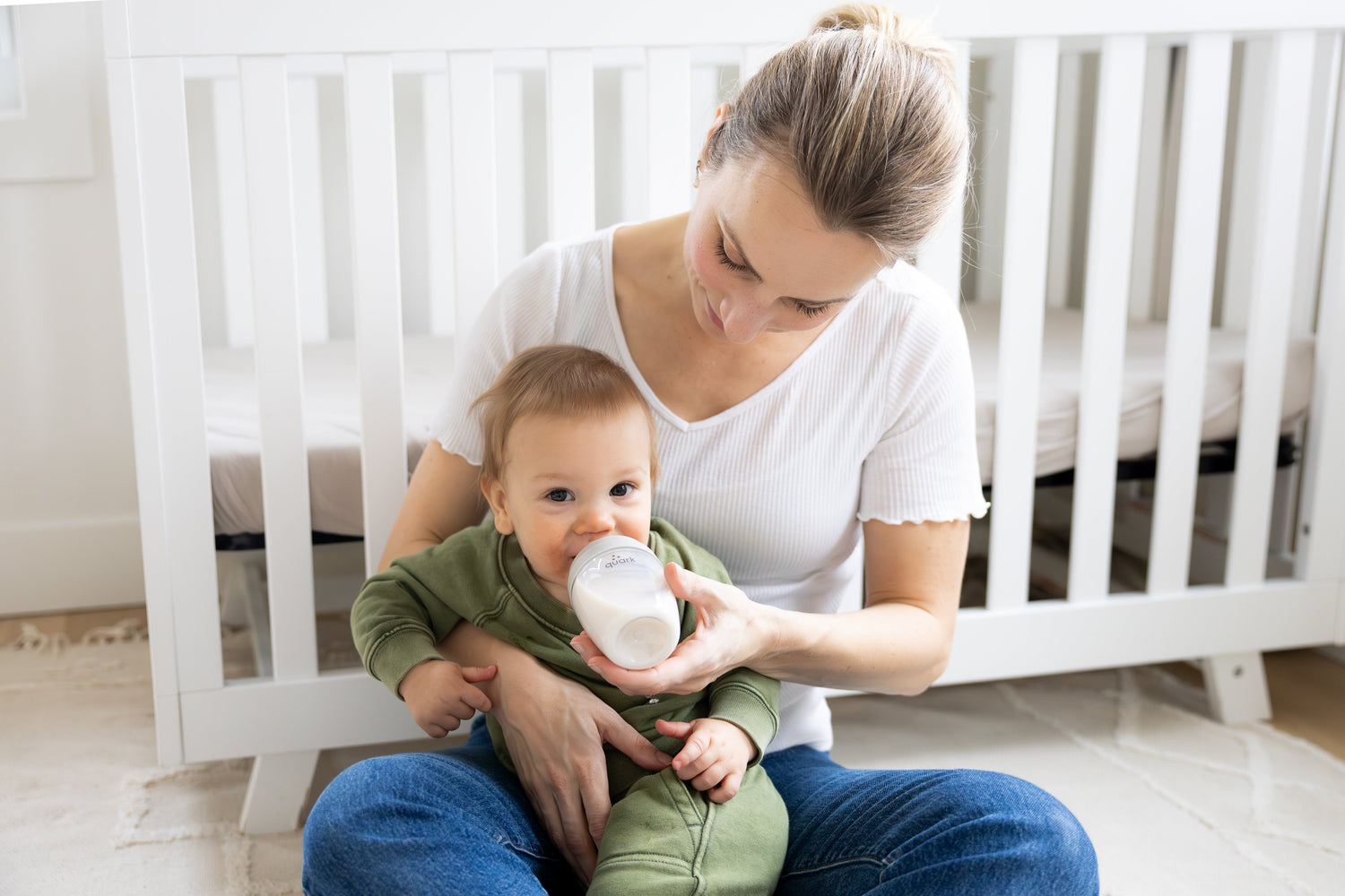 Mother feeding infant with Quark Baby bottle in nursery setting