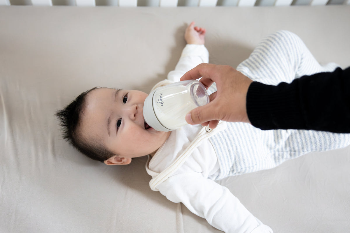 Adult feeding infant Quark Baby bottle in lifestyle shot, breastfeeding support guide