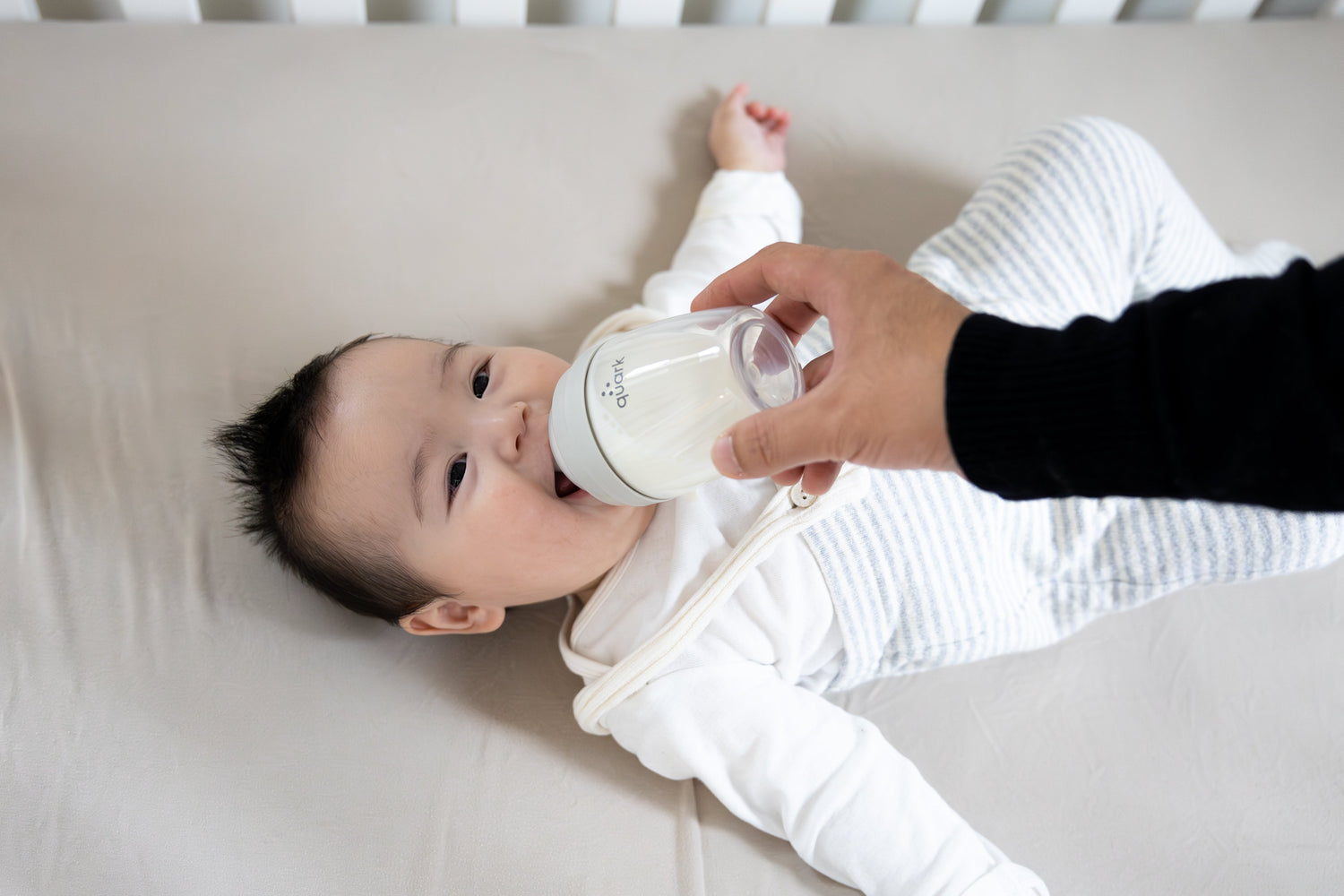 Adult feeding infant Quark Baby bottle in lifestyle shot, breastfeeding support guide