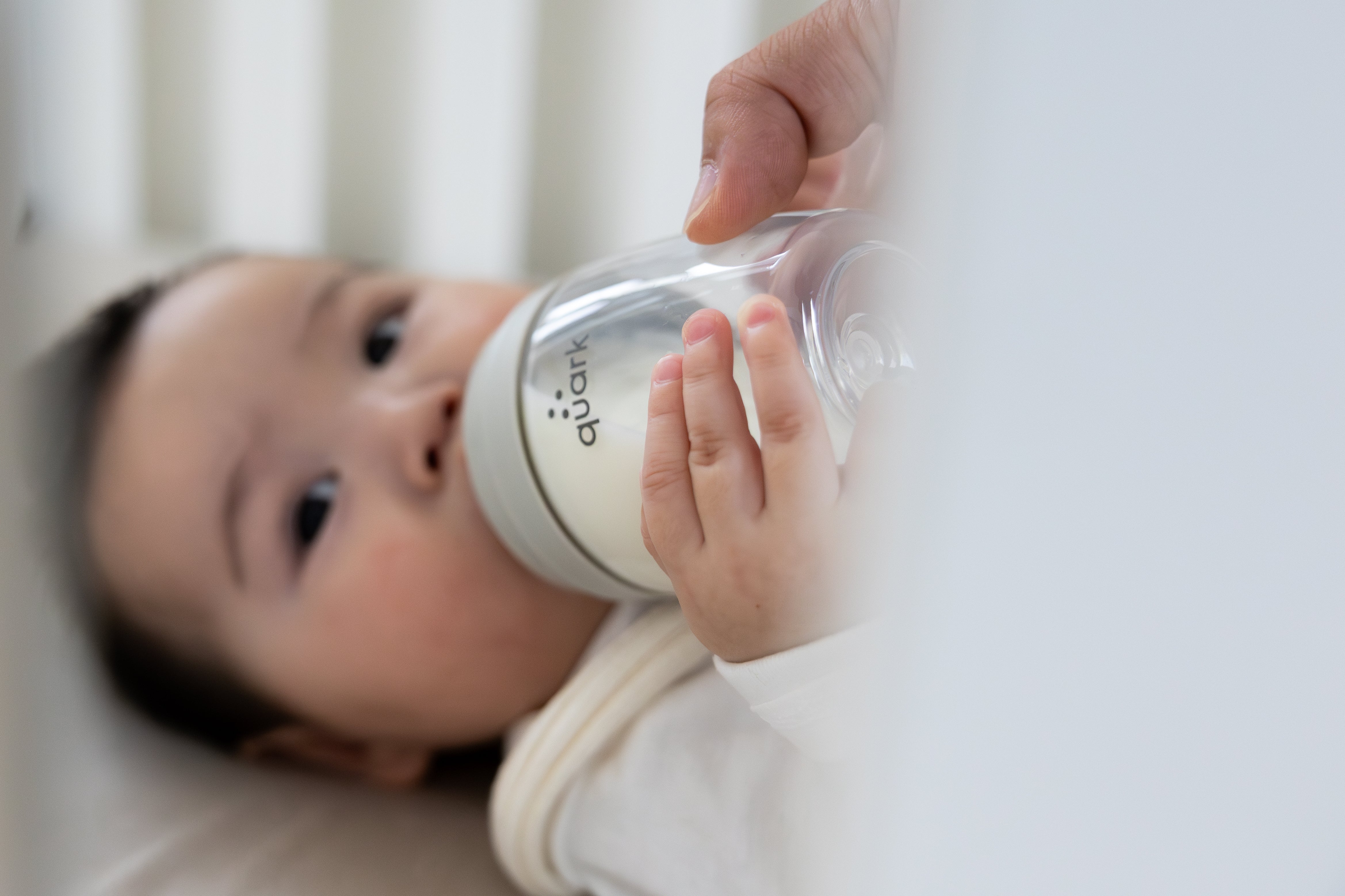Newborn holding Quark Baby bottle with both hands during feeding