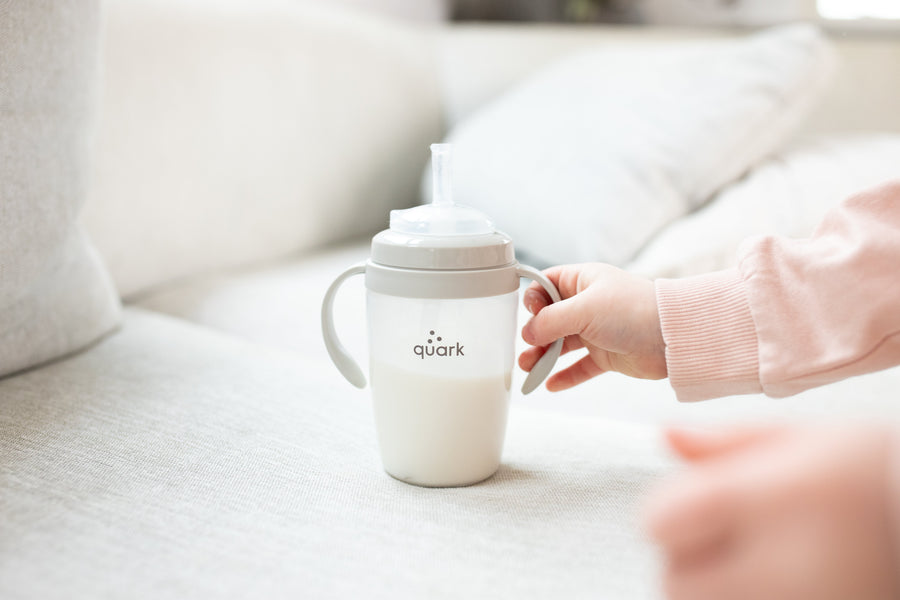 Adult hand presenting Quark Baby BuubiBottle sippy cup with handles on neutral nursery background.