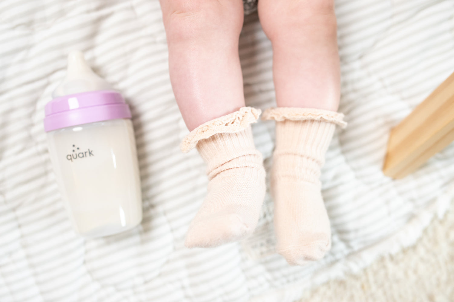 Quark Baby bottle with purple lid next to infant socks on white textured surface
