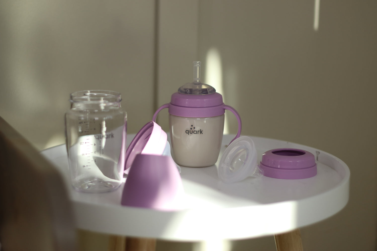 Quark Baby purple sippy cup with handles and accessories on white table.