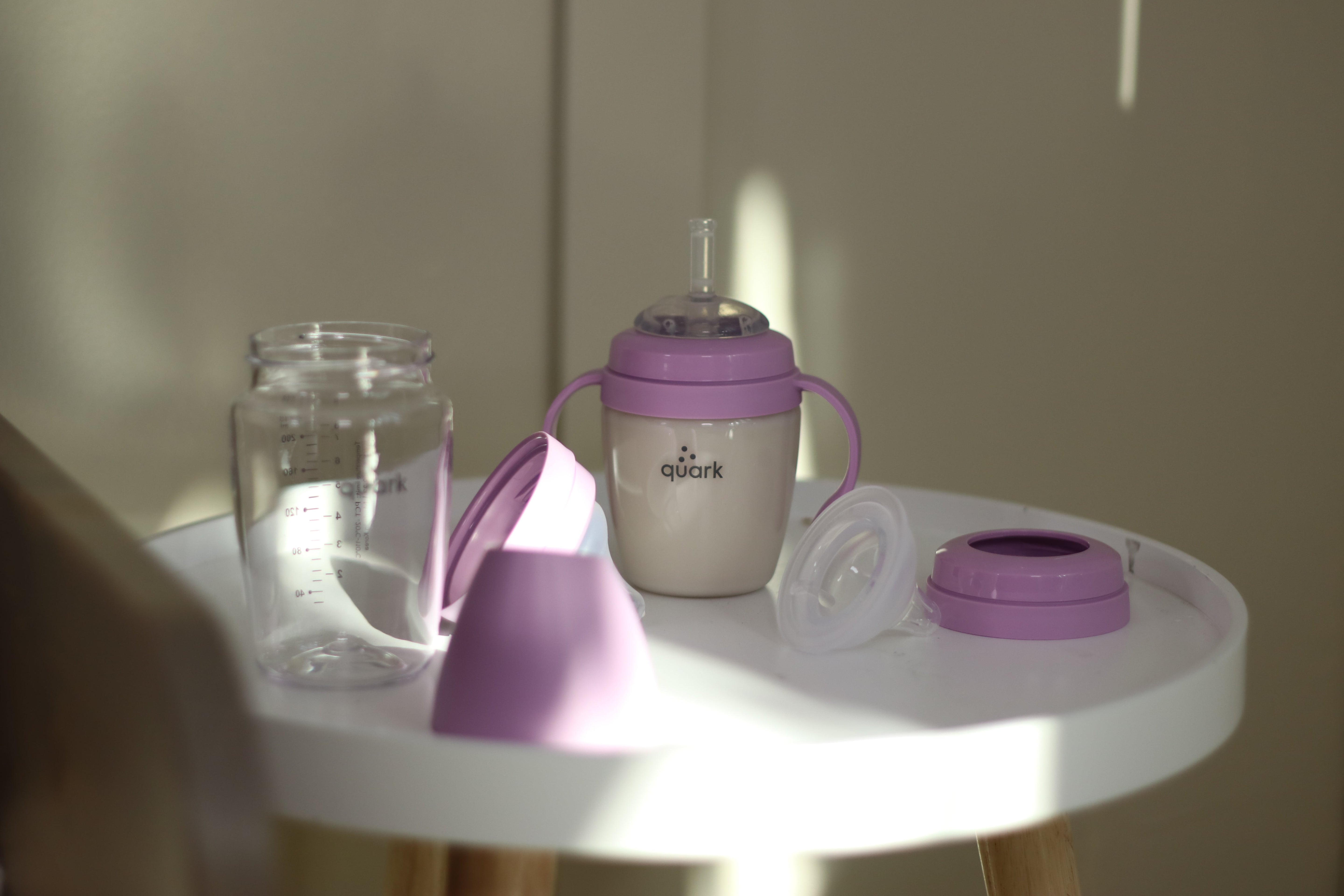 Quark Baby purple sippy cup with handles and accessories on white table.