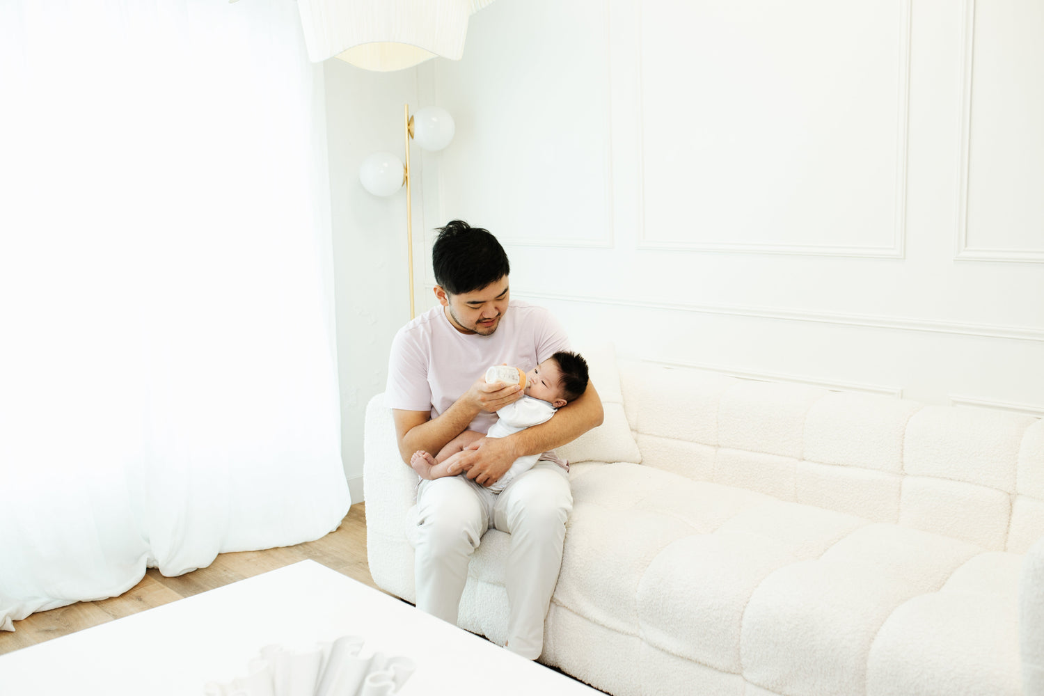 Father feeding newborn infant with Quark Baby bottle in bright nursery setting