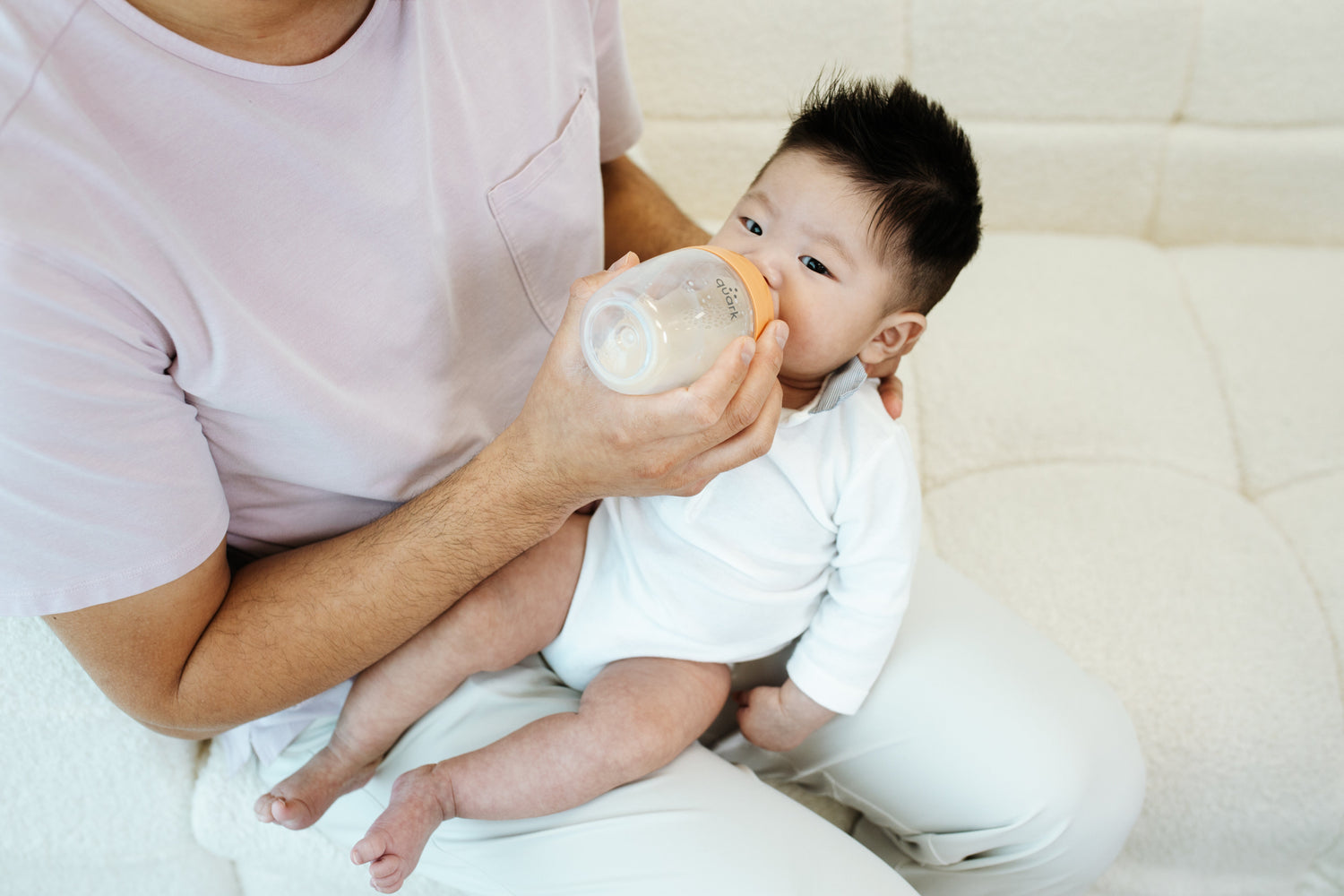 Adult feeding infant Quark Baby bottle during travel, lifestyle scene for stress-free flying guide.