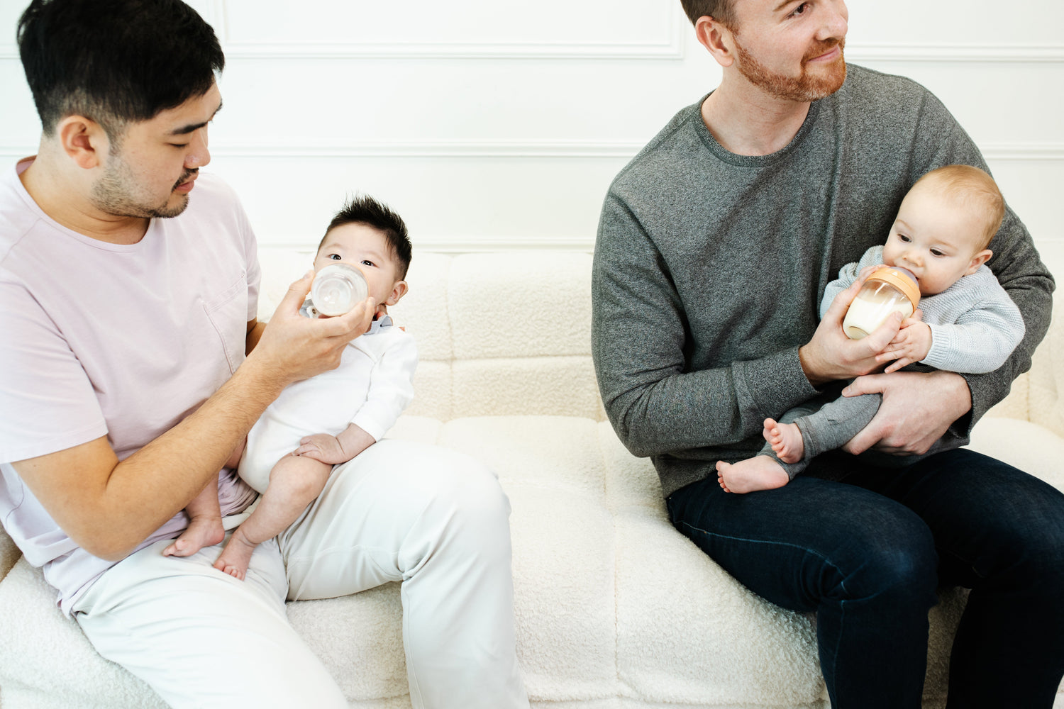 Two fathers bottle-feeding infants with Quark Baby bottles during nursing support session.