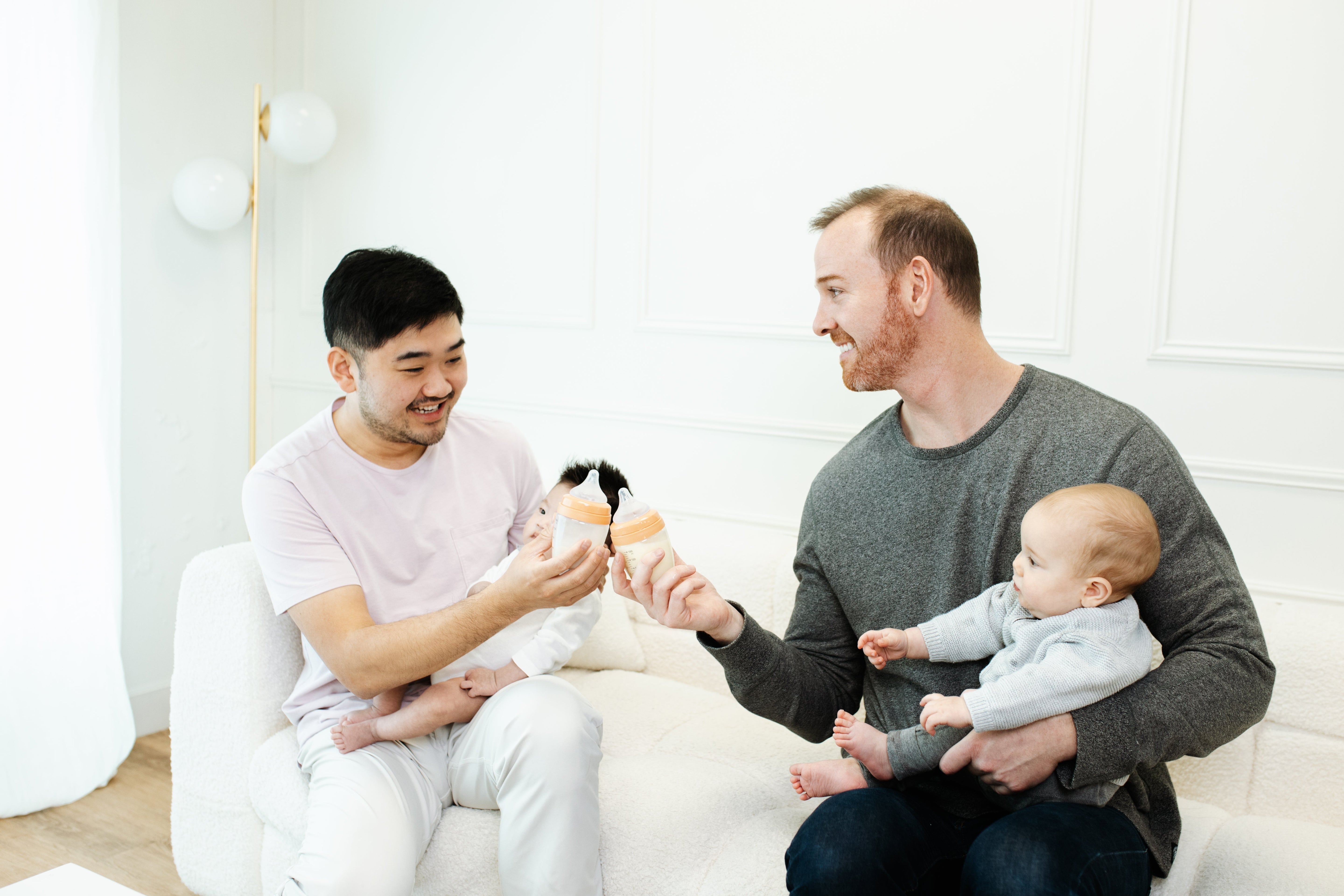 Two men presenting Quark Baby toy to infant in bright, modern nursery setting.