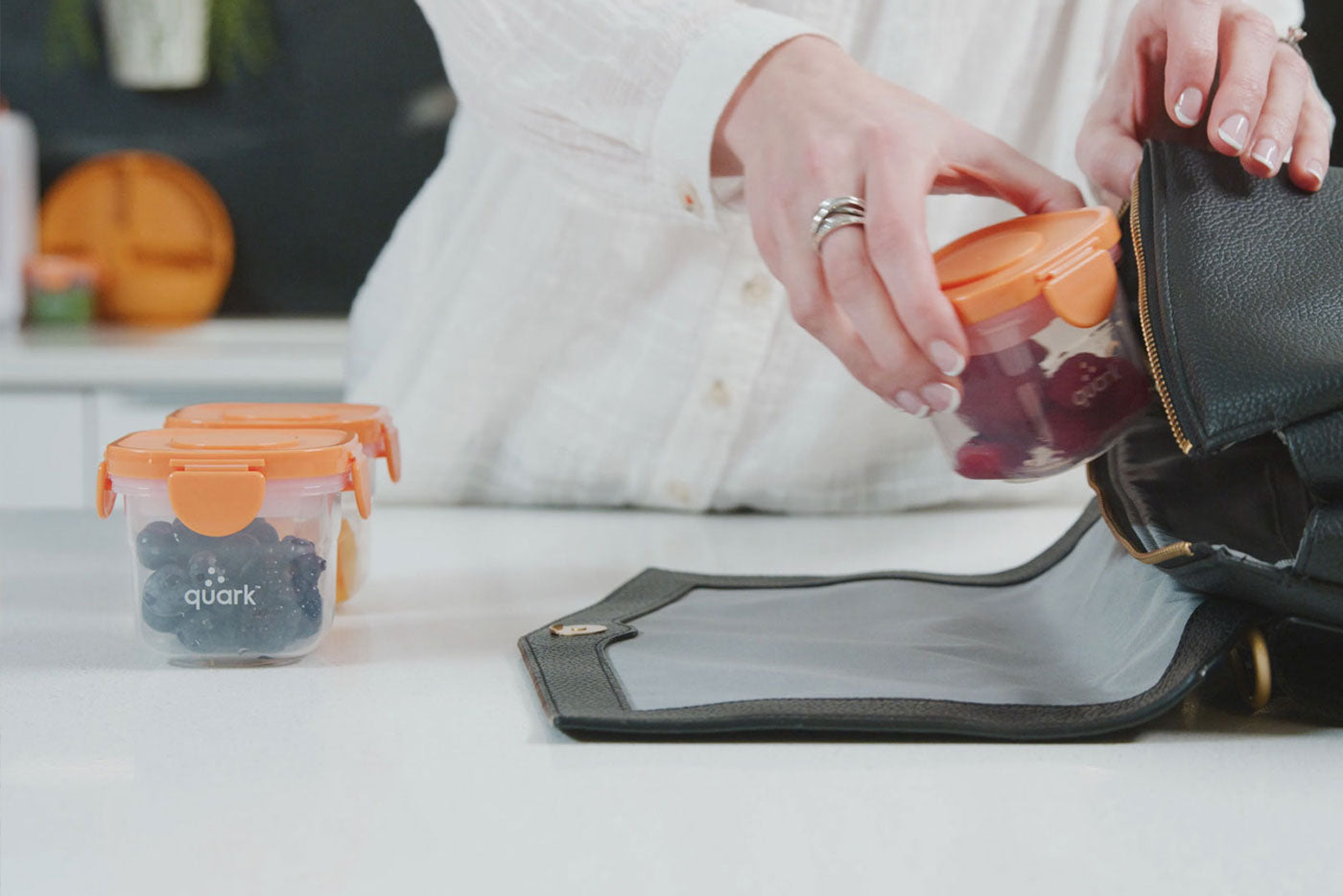 Woman holding Quark Baby orange container with blueberries, lifestyle shot with wallet and orange in background.