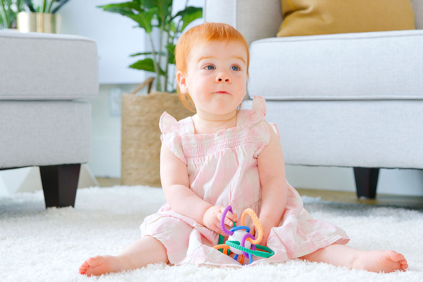 Toddler in pink dress playing with colorful Quark Baby sensory toy on white rug.