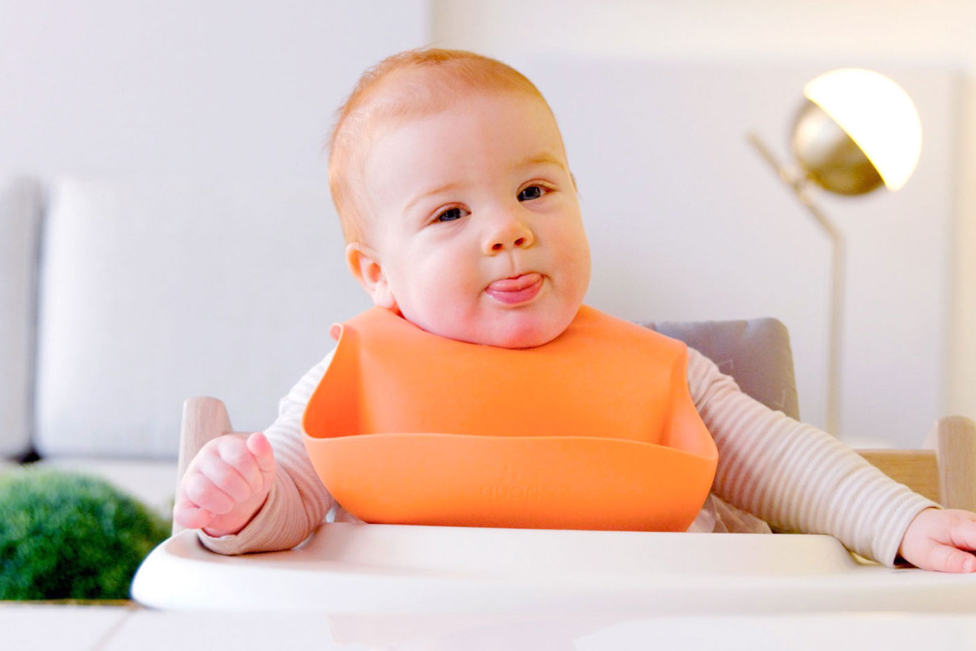 Happy baby in orange bib enjoying mealtime with Quark Baby feeding essentials