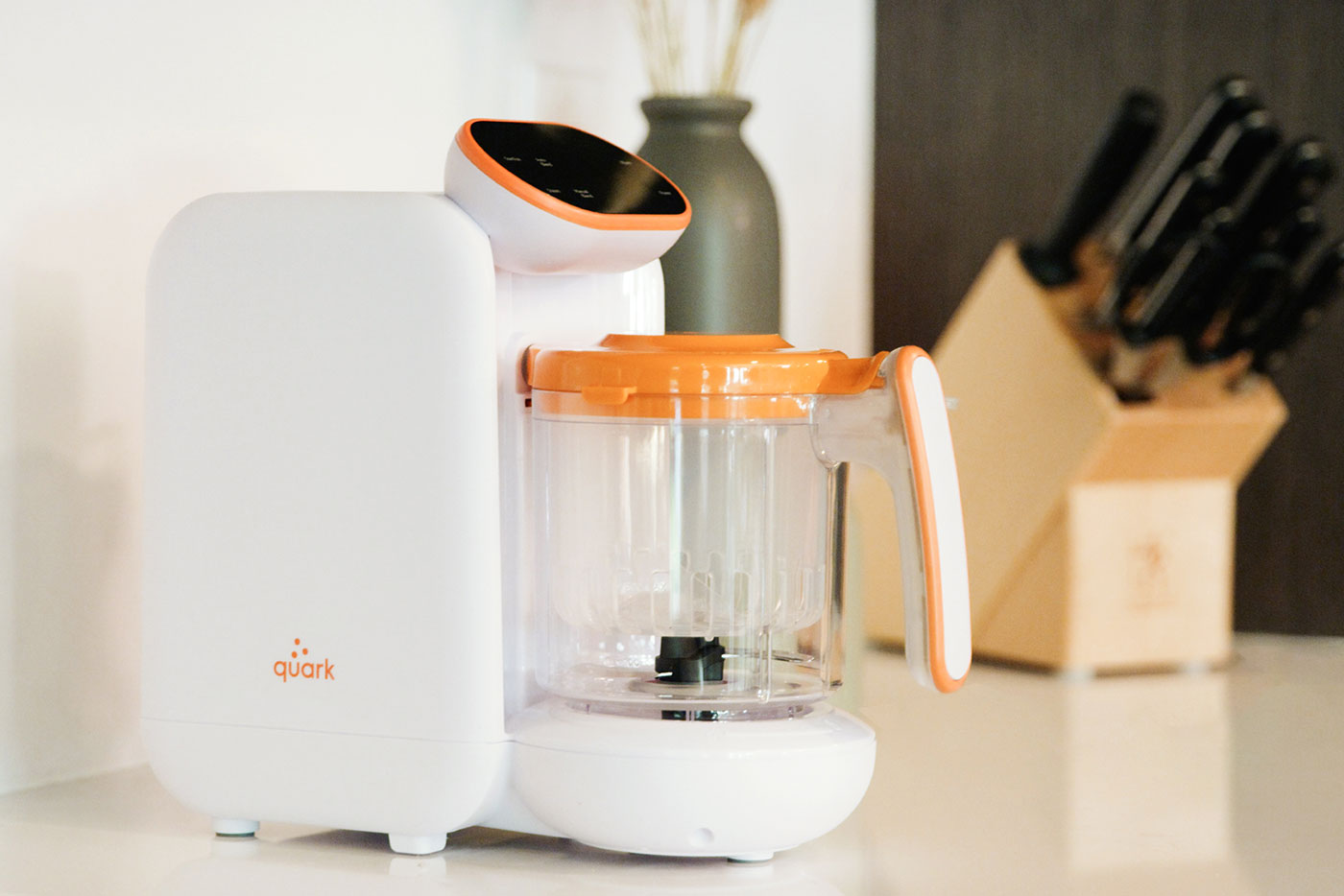 Quark Baby Quook 5-in-1 baby food maker with orange accents on kitchen counter.