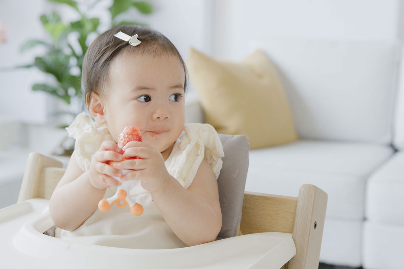 Toddler eating strawberry while sitting in Quark Baby high chair, lifestyle scene