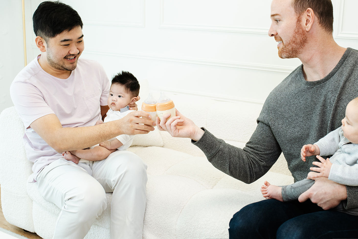 Two fathers sharing Quark Baby bottles while bonding with infants in home setting.