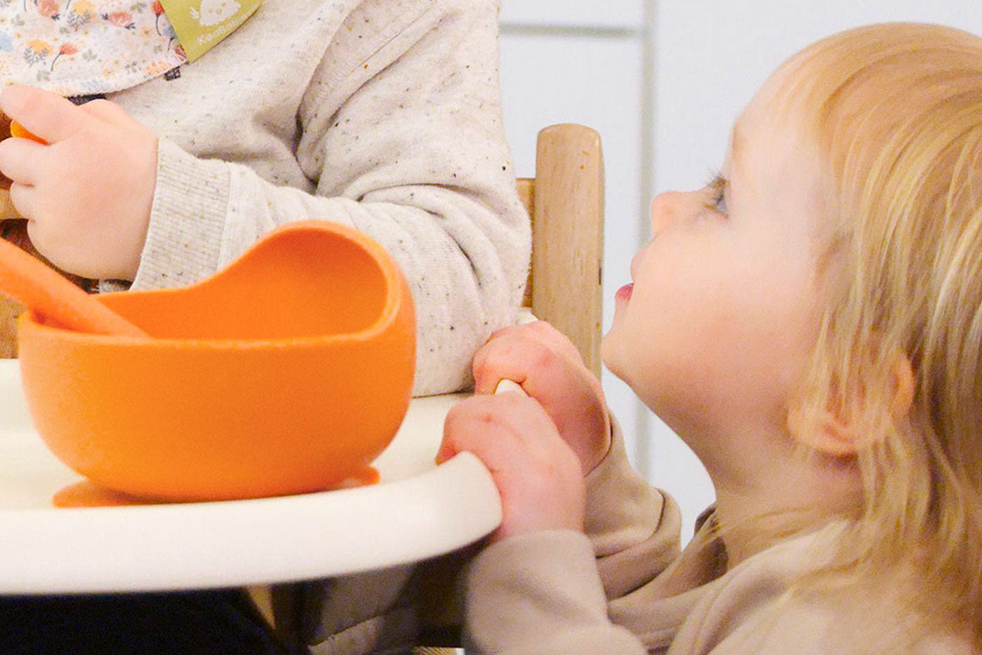 Adult feeding infant from orange Quark Baby bowl during solid foods introduction.