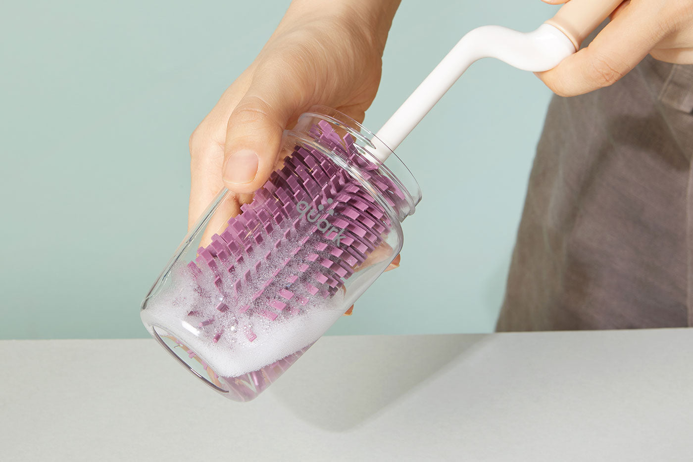 Quark Baby sterilizer cover with purple basket insert being rinsed under water.