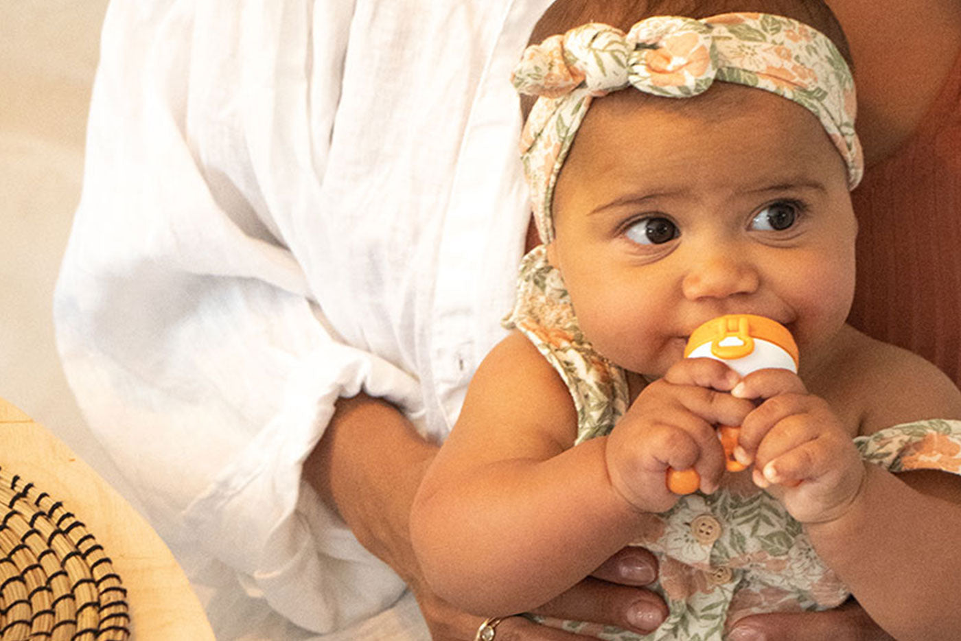 Baby in patterned headwrap and outfit chewing on Quark Baby bottle during feeding, lifestyle portrait.