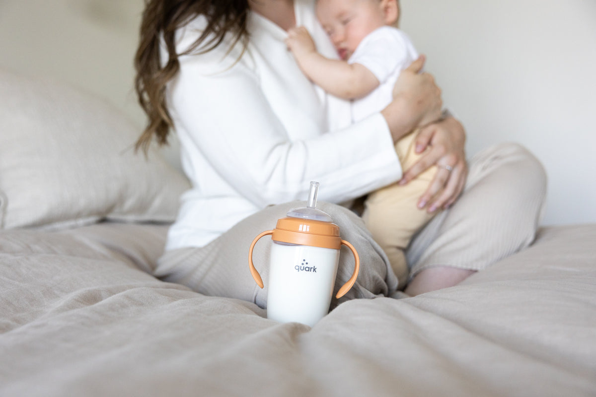 Quark Baby BuubiBottle orange sip kit with adult holding infant during feeding moment, lifestyle shot.
