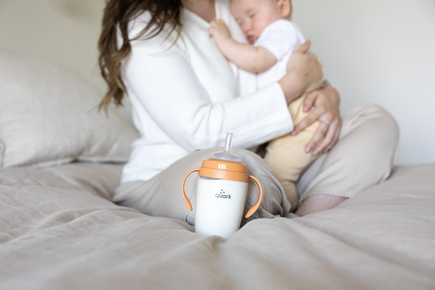Quark Baby BuubiBottle orange sip kit with adult holding infant during feeding moment, lifestyle shot.