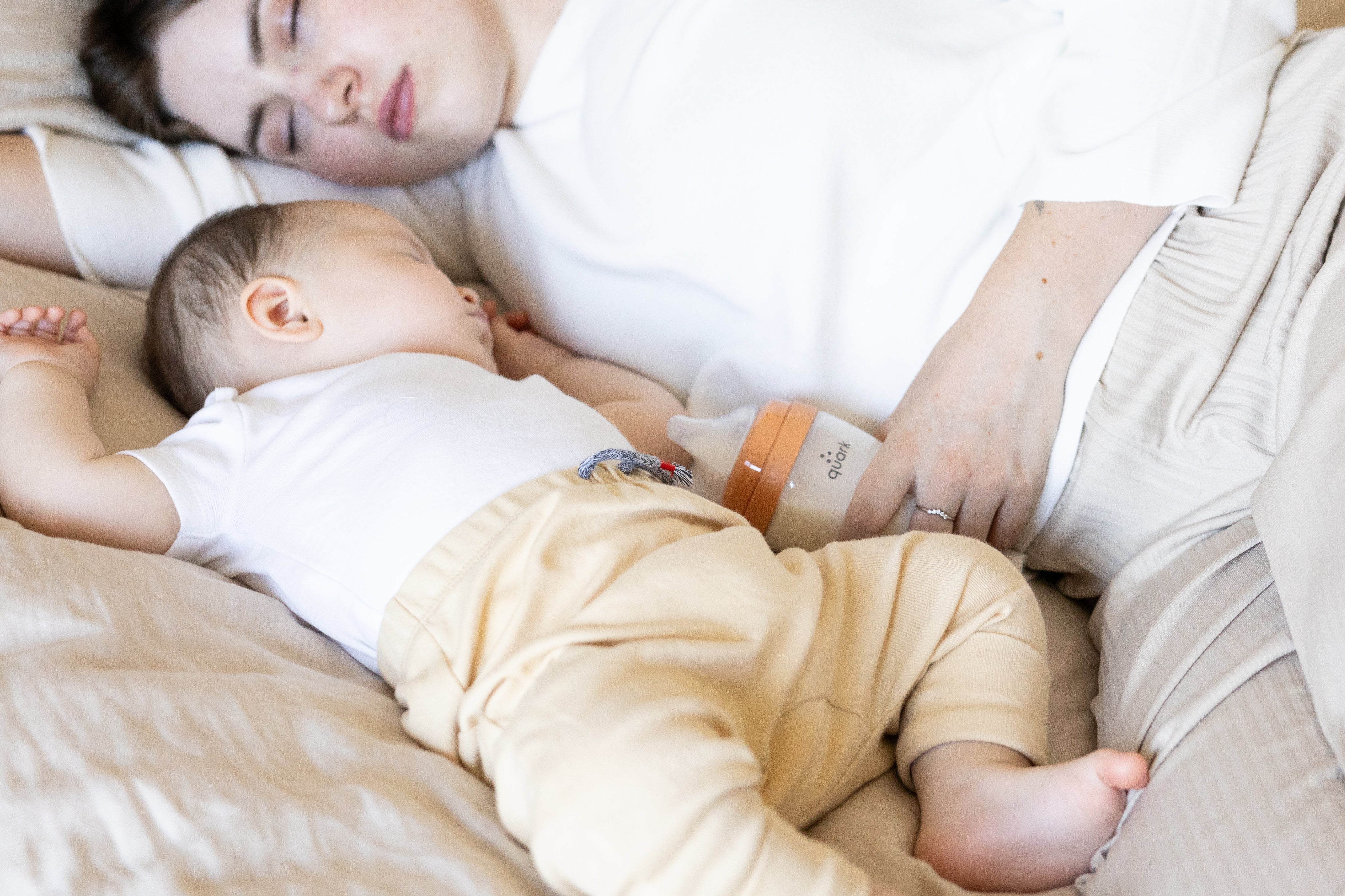 Mother sleeping with infant holding Quark Baby BuubiBottle orange bottle for feeding.