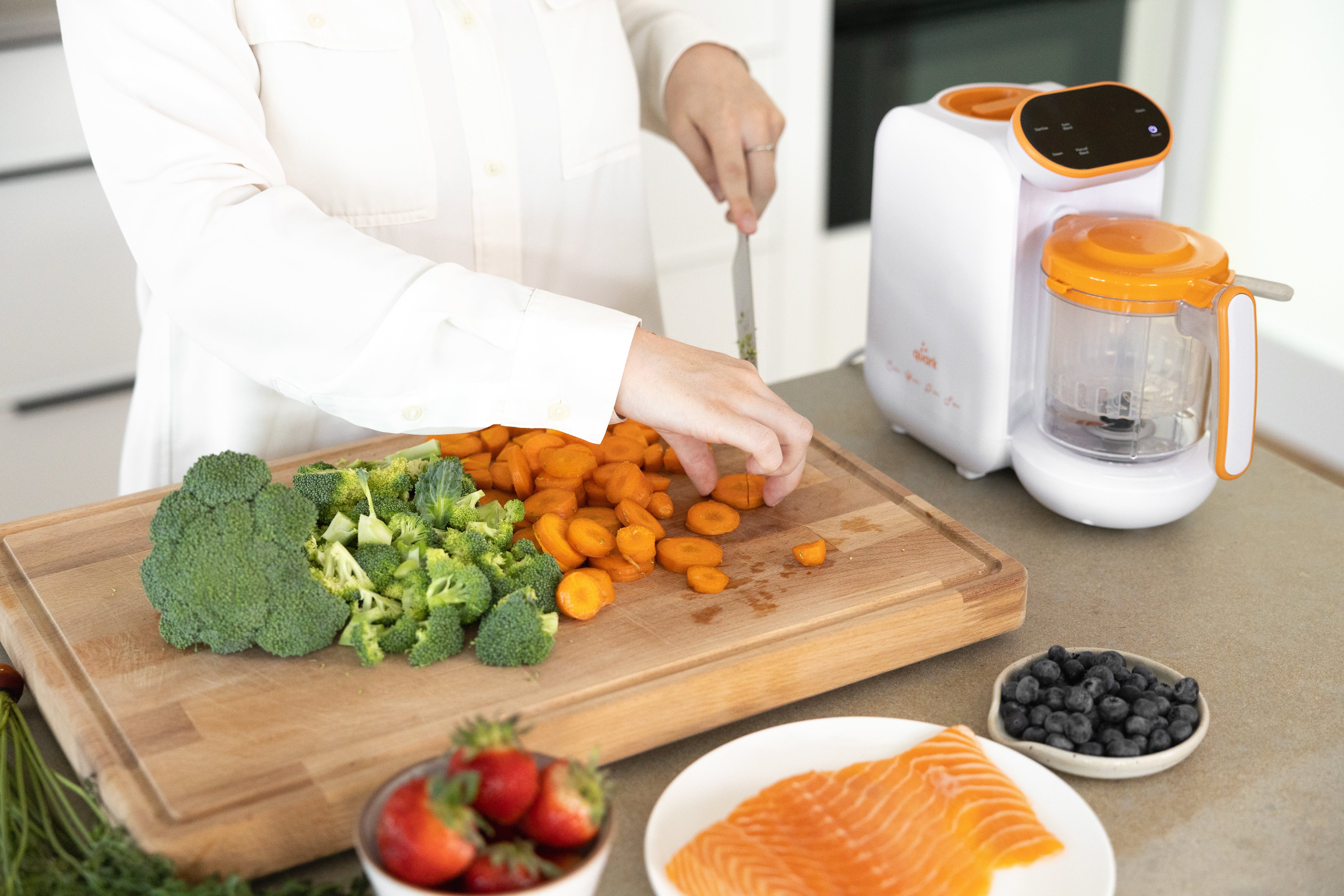 Woman preparing vegetables with Quark Baby Quook food maker for baby-led weaning meal prep.